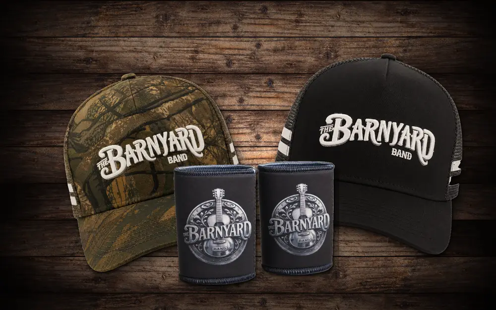 The Barnyard Band camo and black trucker caps with two Barnyard magnet stubby coolers on rustic timber
